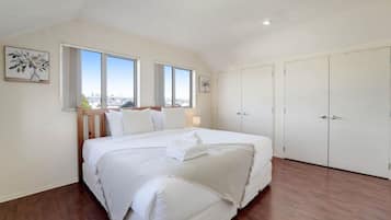 A bedroom with a large bed, two windows, a wardrobe, and a painting on the wall.