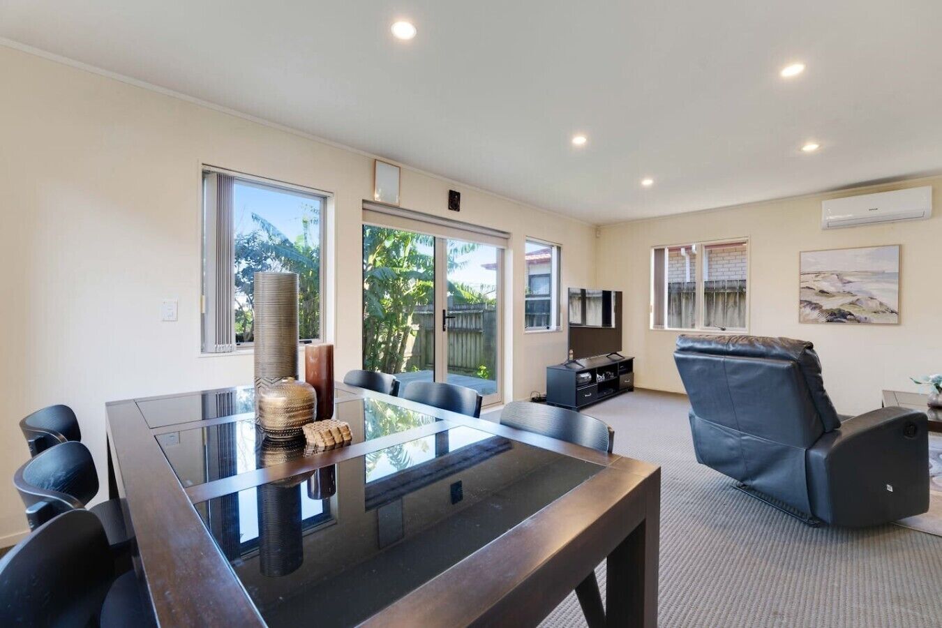 A modern living room with a glass-top table, leather sofa, and a flat-screen TV.