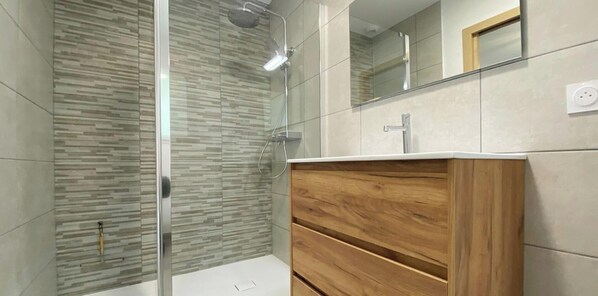 Une salle de bain moderne avec une douche à parois de verre, un meuble-lavabo en bois et un grand miroir.