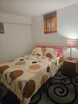 Ein Bett mit gemustertem Überwurf, eine Nachttischlampe, ein Nachttisch und ein Wandbild.