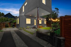 Ein modernes, zweistöckiges Haus mit überdachter Veranda, einem gepflegten Rasen und einer Schotterauffahrt.