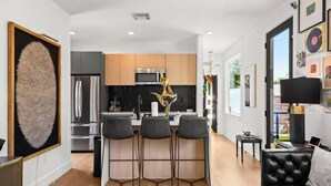 A modern kitchen with a central island, bar stools, and a dining area with a black leather couch. - SoCo Serene Austin Way to Go! (Austin)