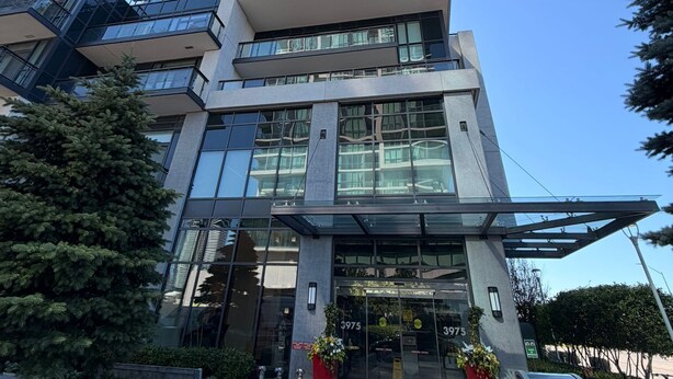 A high-rise building with a modern glass facade, a prominent entrance with a canopy, and a surrounding landscaped area with trees. - Entire Beautiful Apartment in Downtown Mississauga (Mississauga)