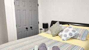 A neatly made bed with striped bedding, a grey door, and a bedside table with a lamp. - Modern 2BR Duplex Near Alta Ski & Salt Lake City (Sandy)