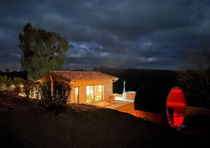 Une petite maison moderne avec un toit en tuiles, de grandes fenêtres et un espace extérieur aménagé, comprenant notamment un jacuzzi.