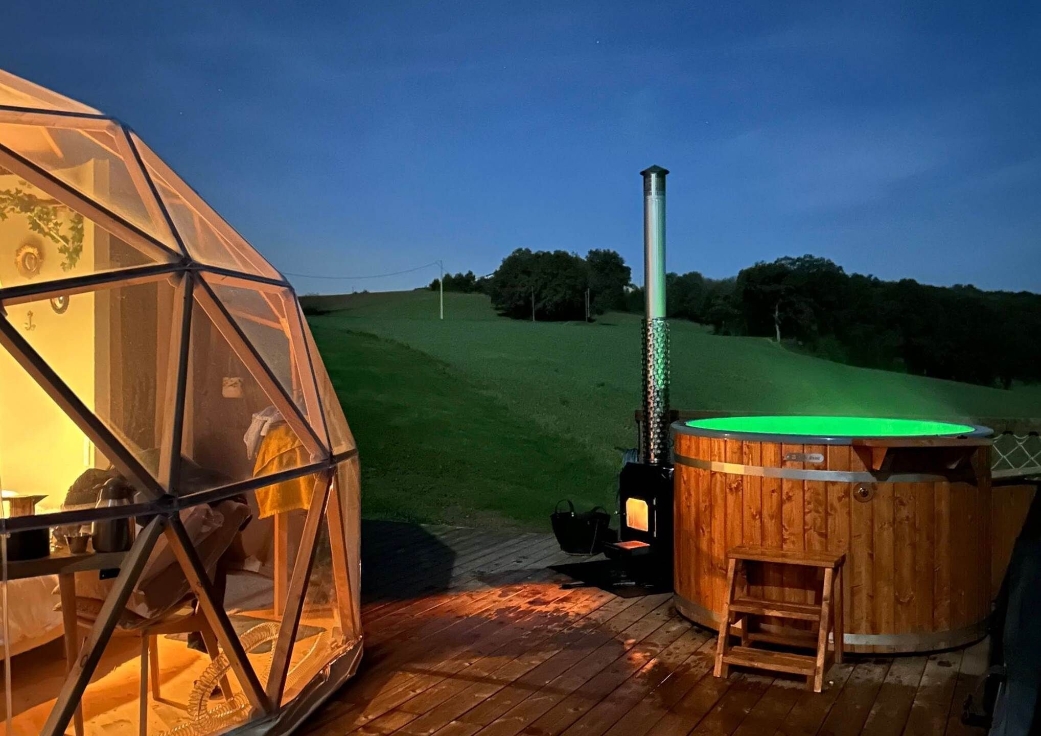 Eine Geodätische Kuppel und ein hölzernes Whirlpool mit Schornstein, beide auf einer Holzterrasse.
