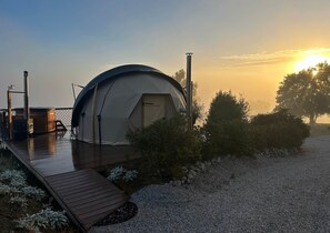 Une tente en forme de dôme dotée d’une terrasse en bois, d’un bain à remous et d’un barbecue.