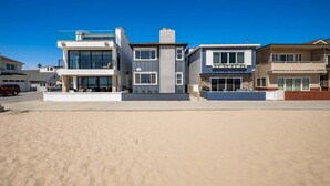 A beachfront property with modern architecture, including a two-story house with a balcony and a garage. - Oceanfront Escape With Direct Beach Access (Newport Beach)