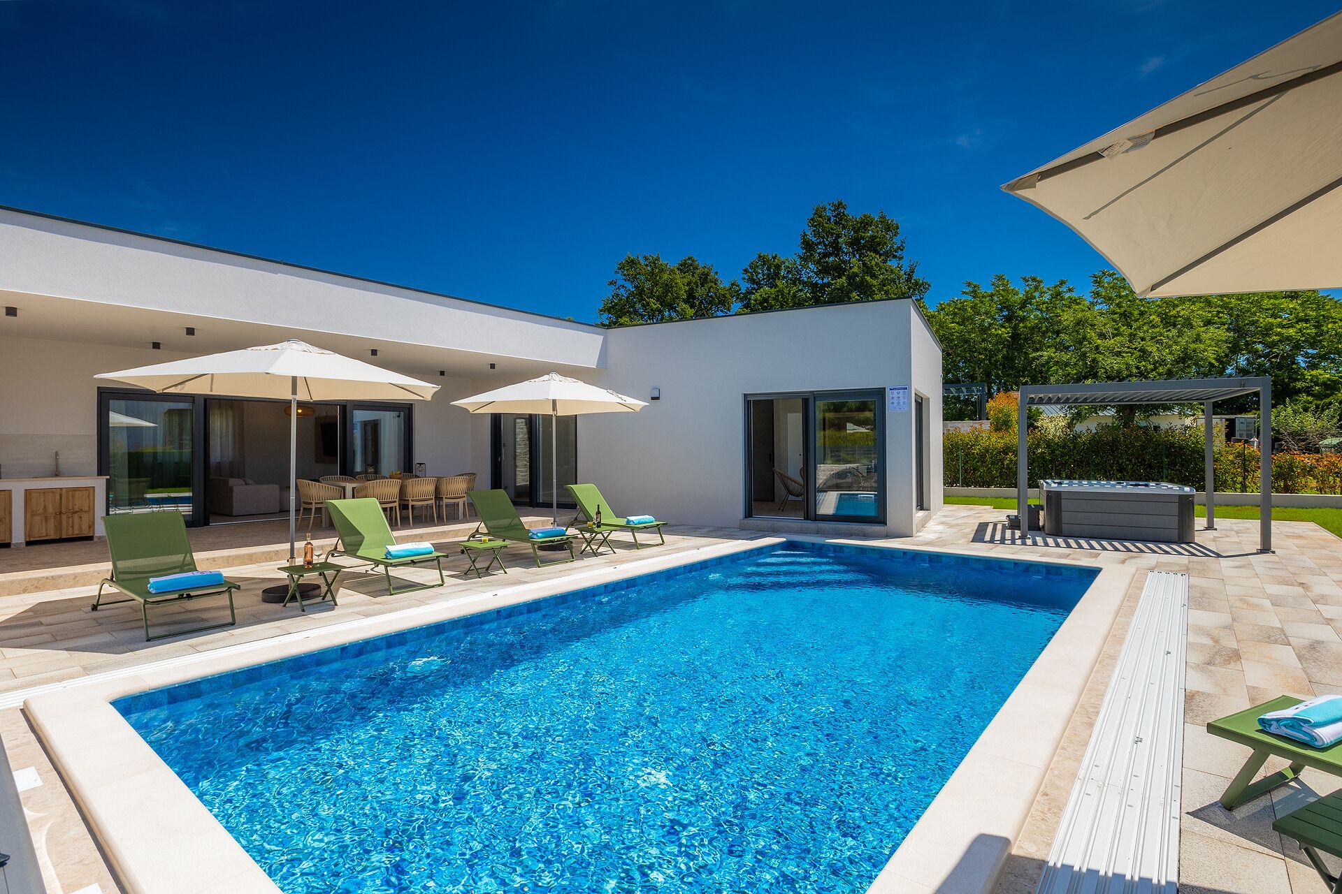 Un espace piscine extérieur moderne, doté de chaises longues, de parasols et d’un jacuzzi.