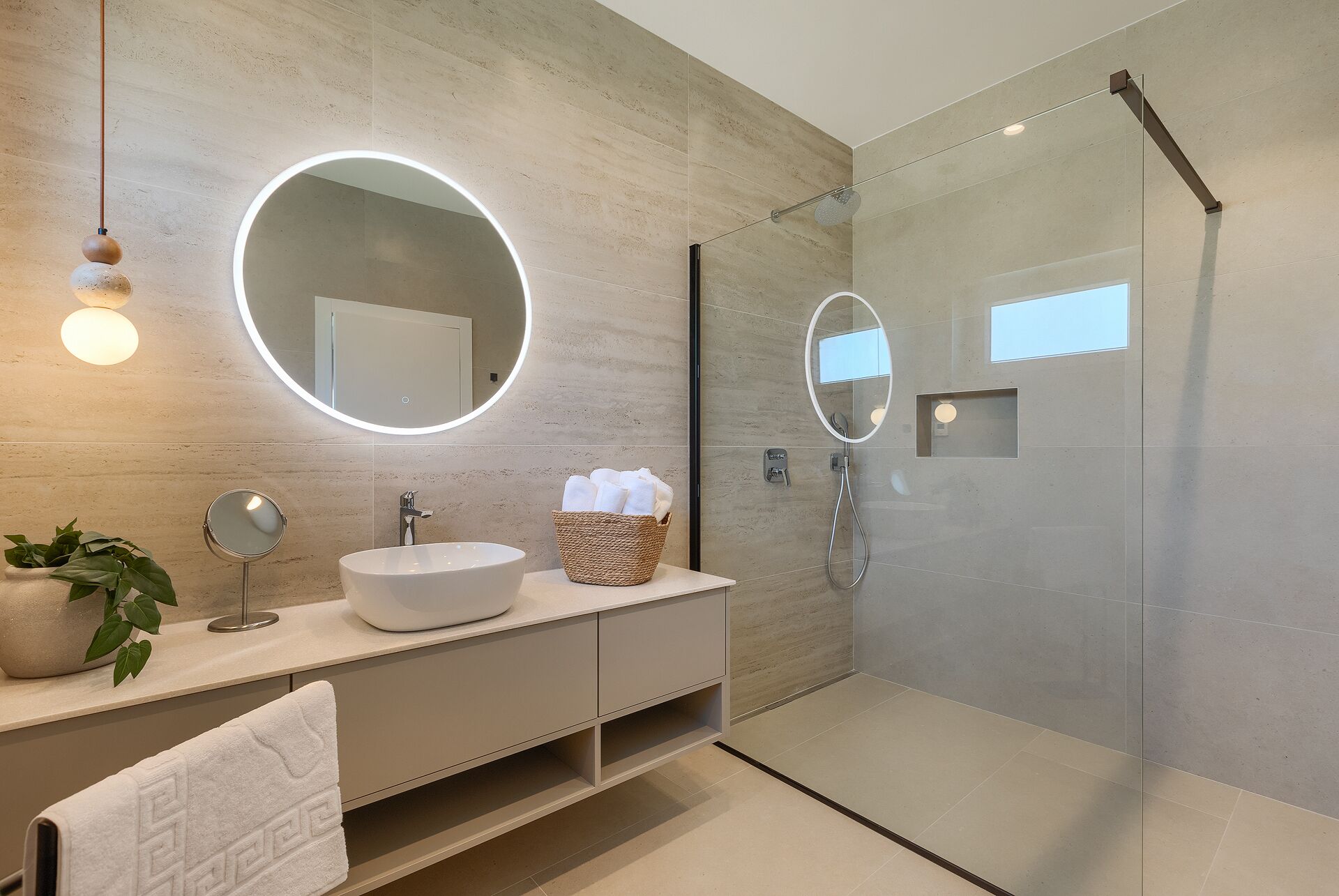 Une salle de bain moderne avec un miroir rond, un lavabo, une douche et une plante en pot.