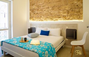 A bedroom with a bed, a bedside table, a chair, a window, and a stone wall. - Minerva Royal Suite - Alghero (Alghero)