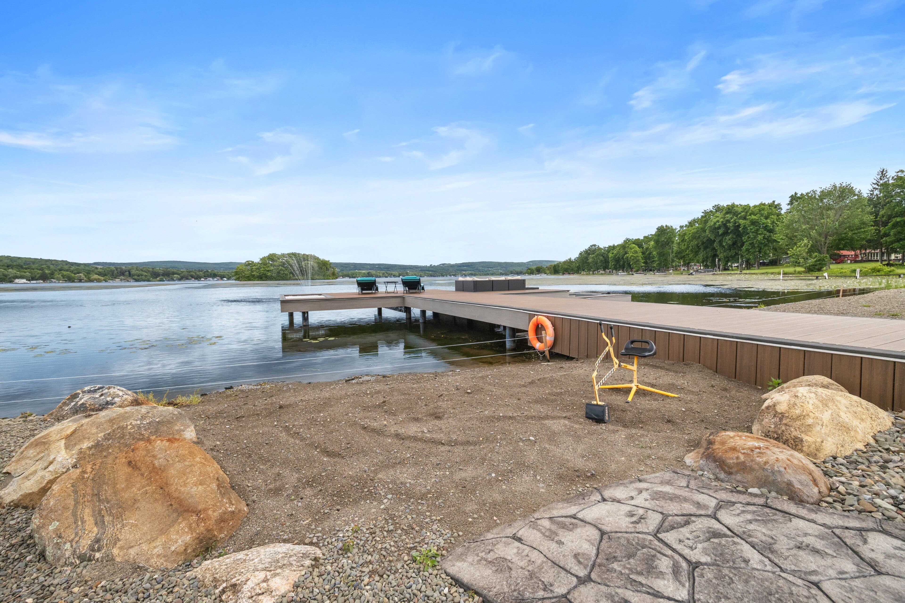 A lakeside dock with a wooden platform, two boats, and a lifebuoy.