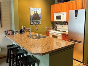 A kitchen with granite countertops, a stainless steel sink, a microwave, a stove, and a refrigerator.