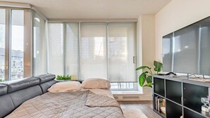 Une chambre moderne avec un grand lit, une télévision et une fenêtre donnant sur la ville.