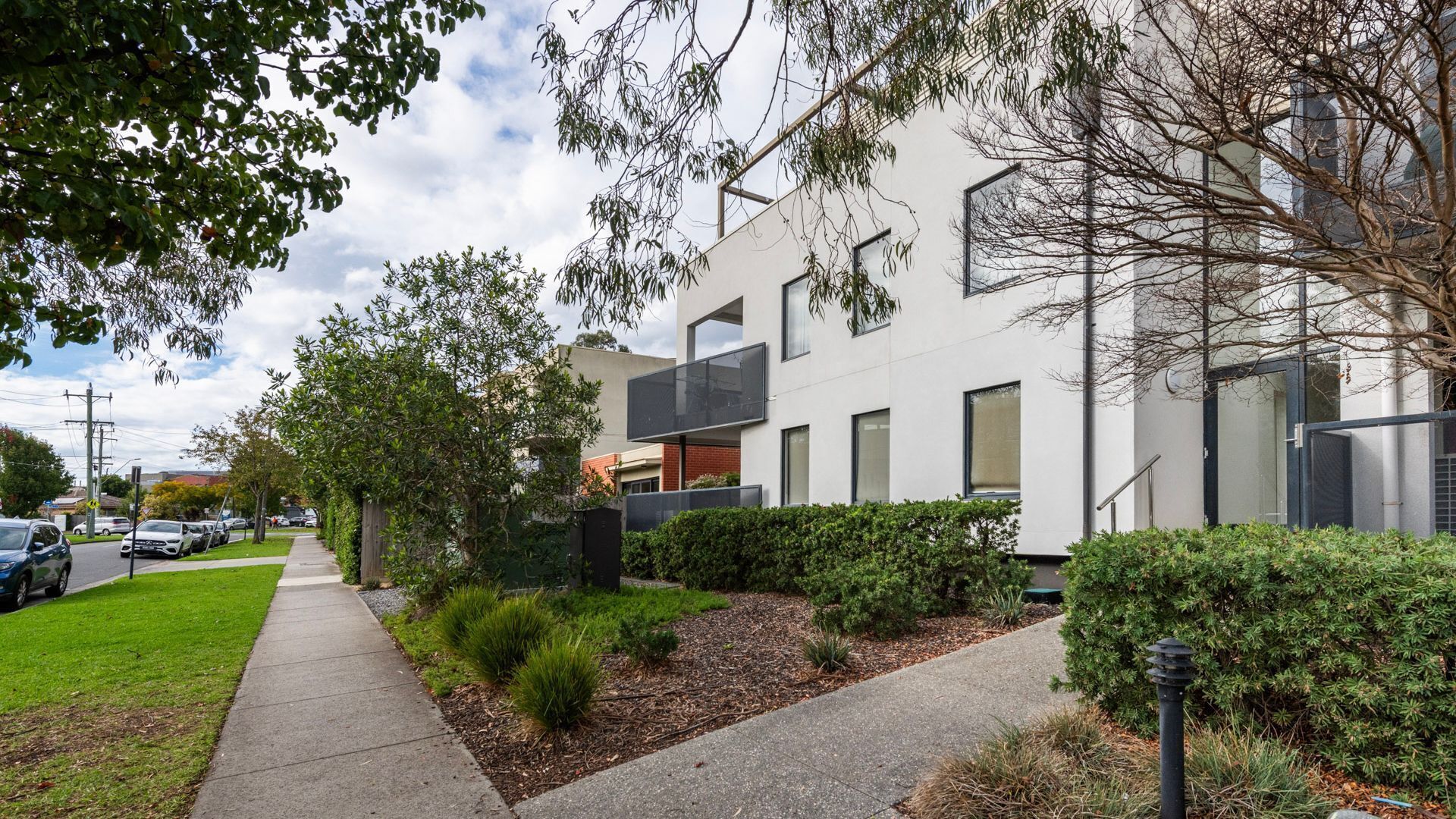 A modern residential building with a paved driveway, a well-maintained lawn, and mature trees.