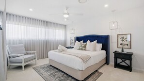 A bedroom with a bed, a chair, a nightstand, a ceiling fan, and a window with curtains. - Glass House Escape at Forresters (Forresters Beach)