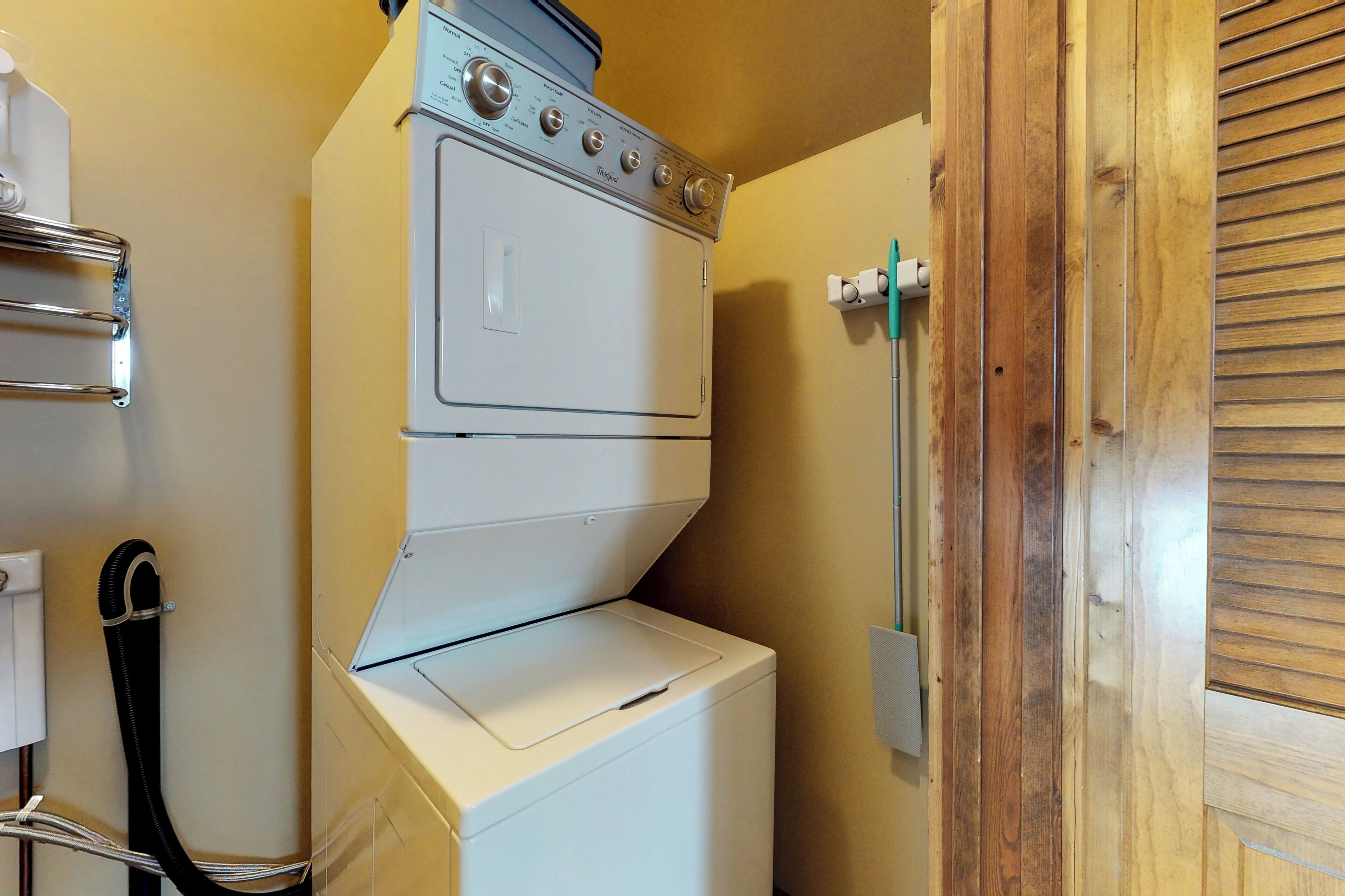 Un espace buanderie compact comprenant un lave-linge et un sèche-linge superposés, un étendoir métallique et une porte en bois.