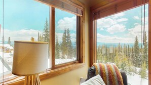 Quarto com uma janela grande que oferece vista para árvores e montanhas cobertas de neve.