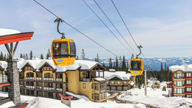 Estância de esqui com teleféricos amarelos, edifícios de madeira e montanhas cobertas de neve ao fundo.