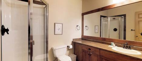 A bathroom with a glass shower enclosure, a toilet, a sink, and wooden cabinets.