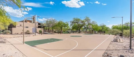 Un terrain de basket en plein air, avec un ciel dégagé, des arbres et un bâtiment en arrière-plan.