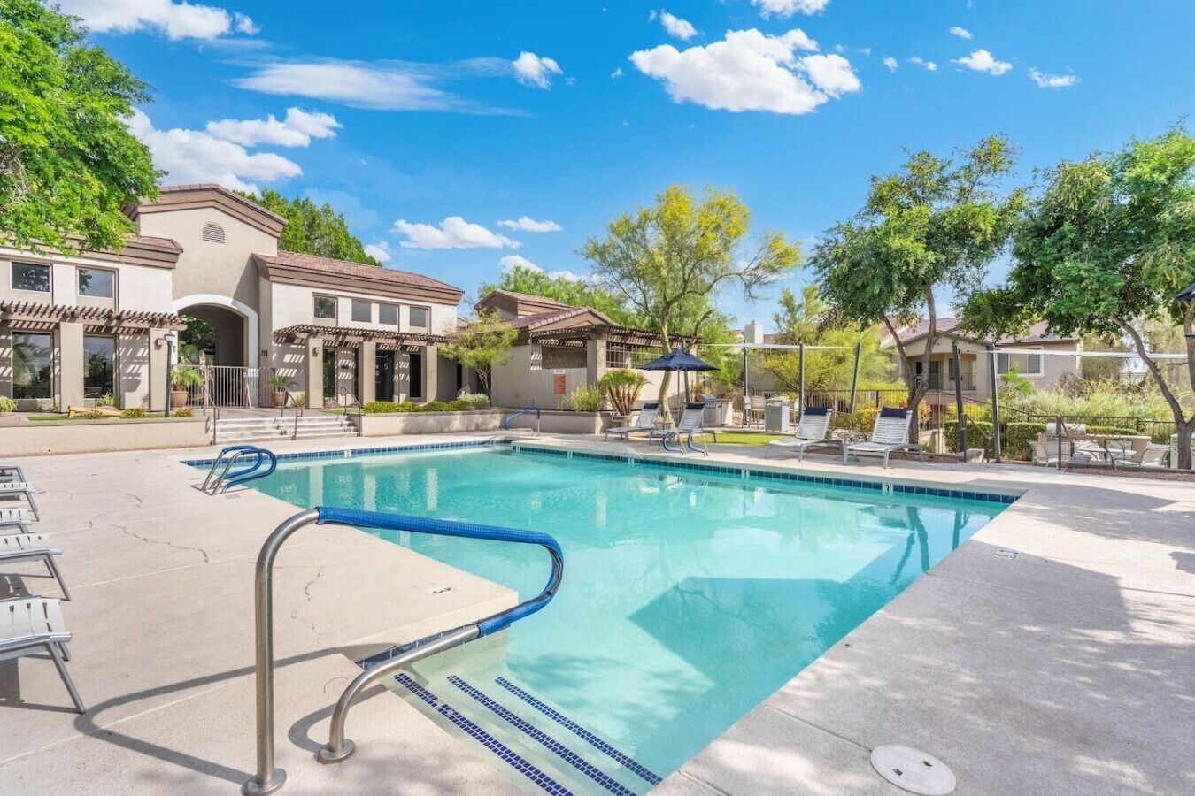 A swimming pool with a blue border, adjacent lounge chairs, and a clear sky.