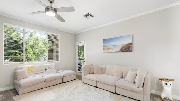 A living room with a sofa, a rug, a ceiling fan, and a painting on the wall.
