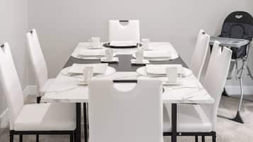 Mesa de jantar posta para seis com cadeiras brancas, um jogo americano preto e pratos e copos brancos.
