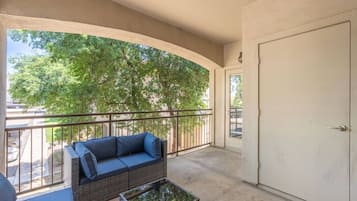 Varanda com sofá, mesa pequena, porta e vista para árvores.