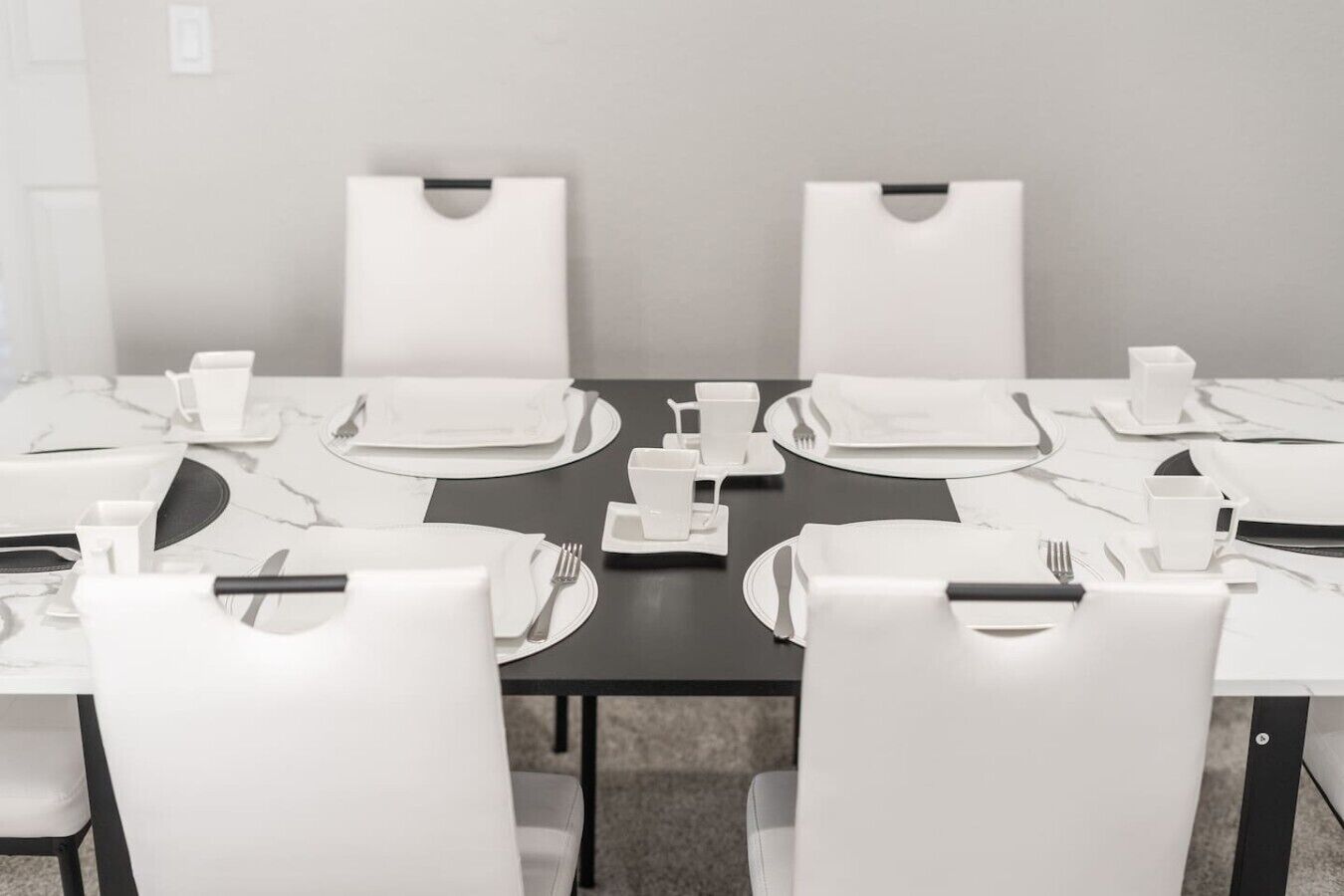 A conference room with a rectangular table, white chairs, and neatly arranged dining tables with plates, cutlery, and cups.