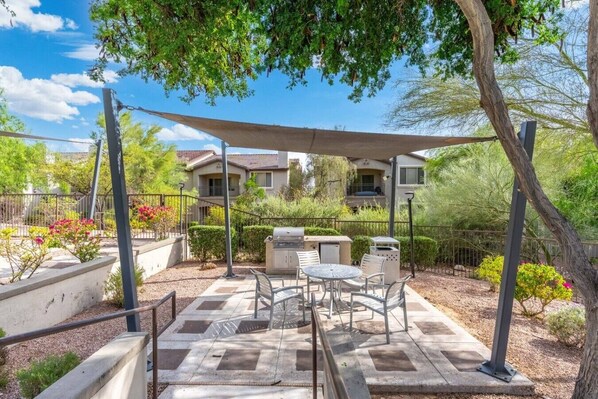 A patio area with outdoor furniture, a barbecue grill, and a shaded canopy.