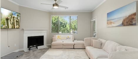 A living room with a fireplace, a ceiling fan, a large window, and a sectional sofa.