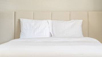 A bed with a headboard, white bedding, and a plain wall.