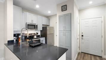 A modern kitchen with white cabinets, a black countertop, stainless steel appliances, and a grey door.