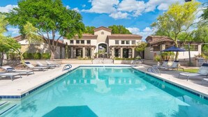 A swimming pool with lounge chairs, a building with a tiled roof, and trees in the background. - Just A Little Comfort (Scottsdale)