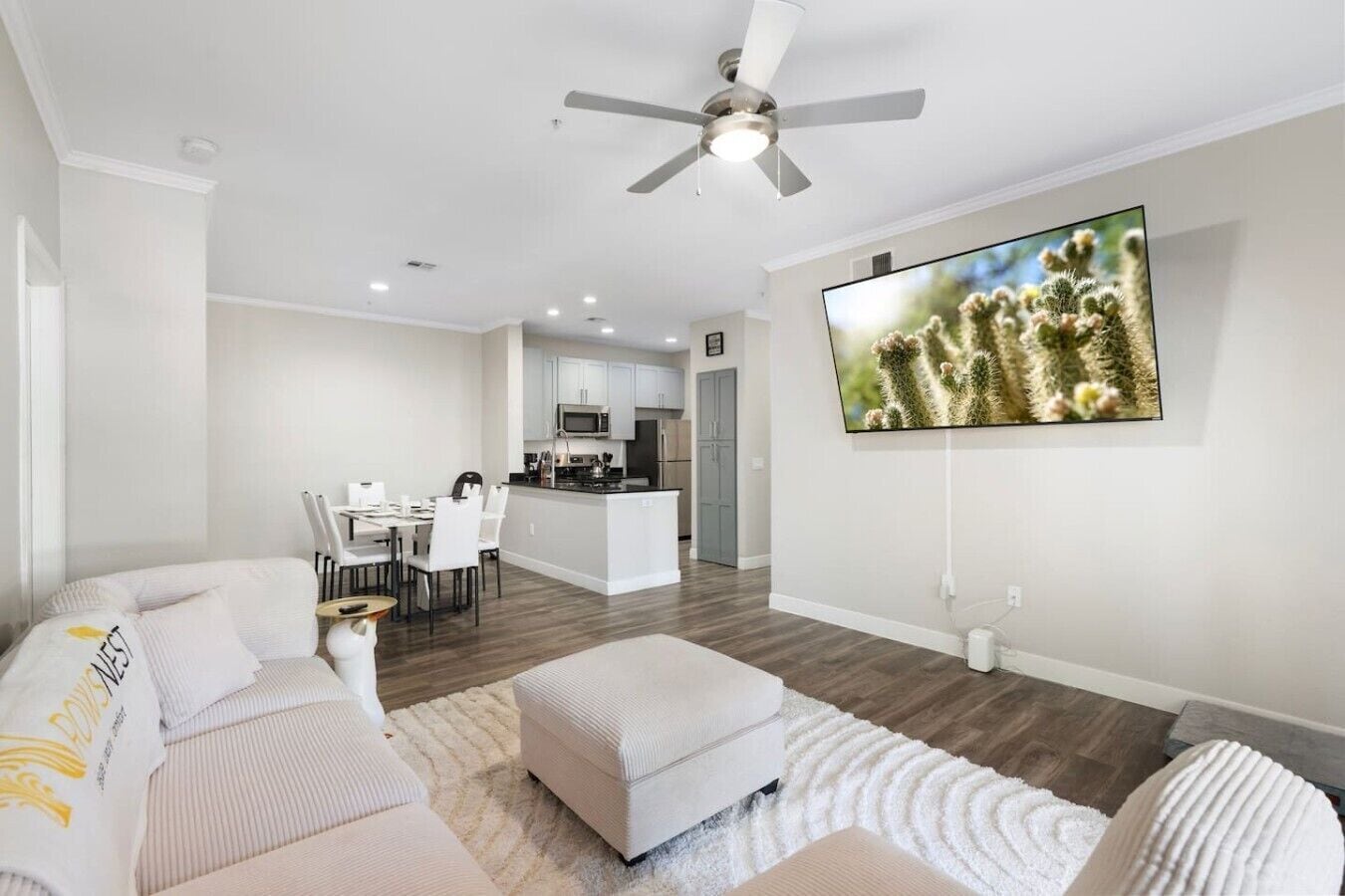 Un salon moderne avec un canapé, un pouf et un téléviseur à écran plat fixé au mur.