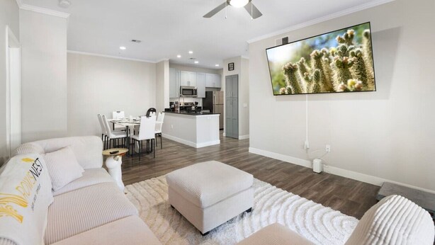 A modern living room with a sofa, ottoman, and a flat-screen TV mounted on the wall. - Just A Little Comfort (Scottsdale)