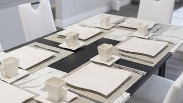 A dining table set with white plates, cups, and cutlery, arranged on a black table runner with a marble-like pattern.