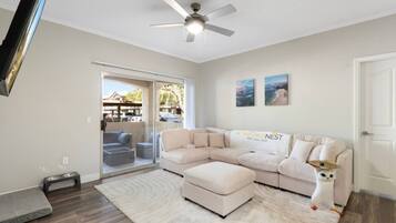 A living room with a sectional sofa, a ceiling fan, a sliding glass door leading to an outdoor area, and a small dog statue.