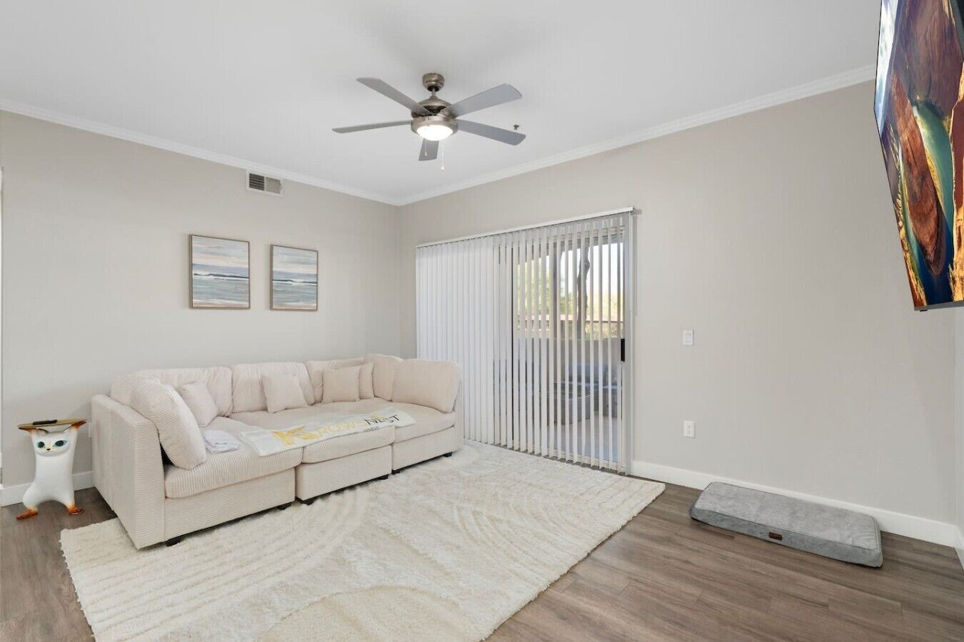 A living room with a beige sofa, a white rug, a ceiling fan, and a sliding glass door.