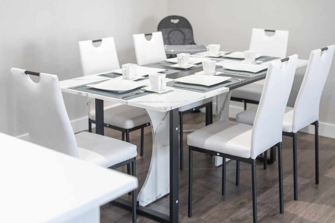 Ein Konferenzraum mit einem weißen Tisch, schwarzem Metallgestell und weißen Stühlen.