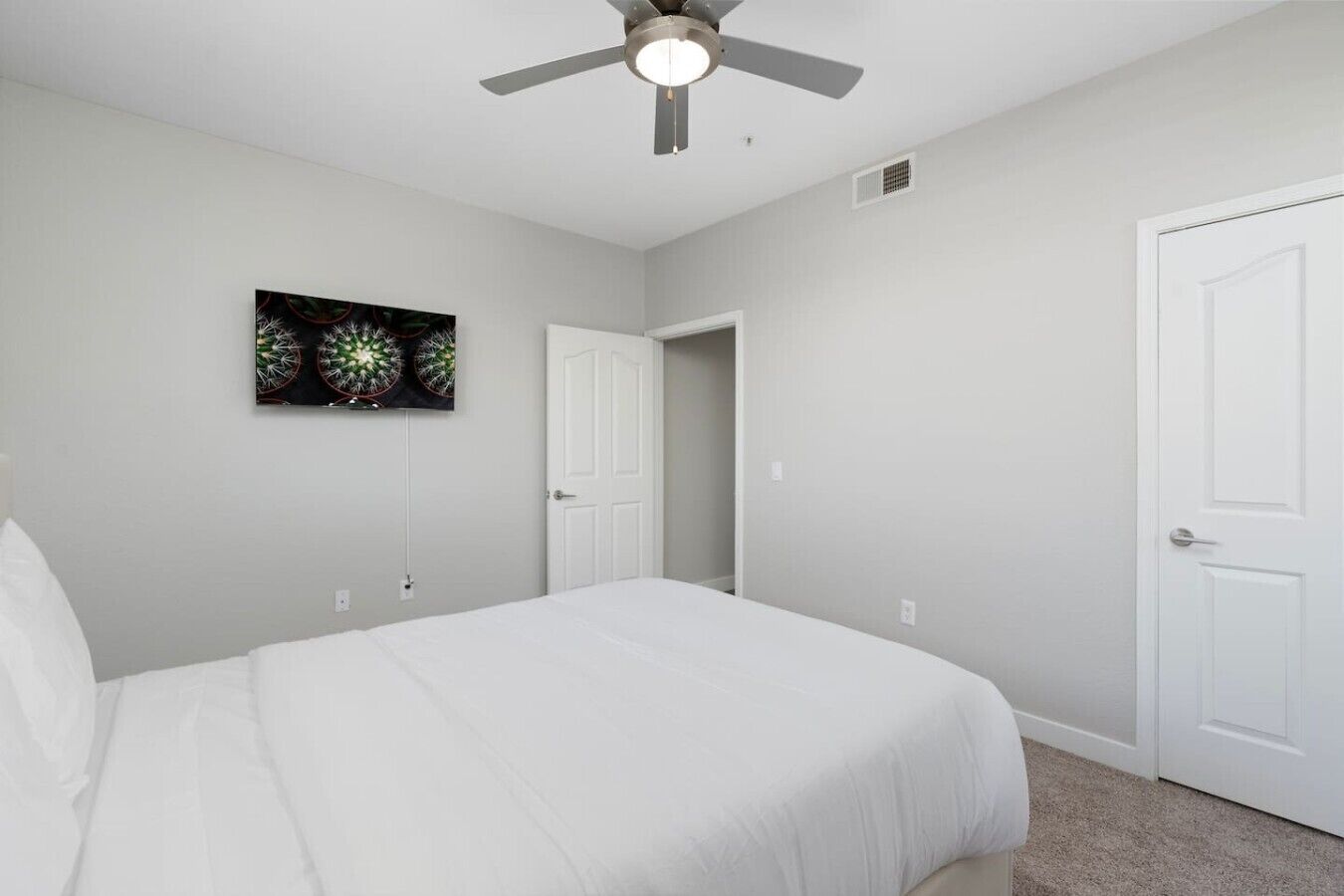 Un dormitorio con cama, ventilador de techo, una puerta y una obra de arte en la pared.