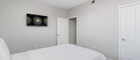 Un dormitorio con cama, ventilador de techo, una puerta y una obra de arte en la pared.