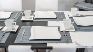 A conference table set with white plates, cups, and cutlery, with a grey placemat underneath. - Your Fun Friendly Stay (Scottsdale)