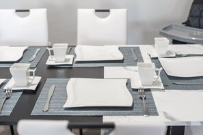 Ein Konferenztisch ist mit weißen Tellern, Tassen und Besteck gedeckt, darunter liegt eine graue Tischmatte.