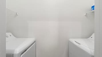 Un lavadero con dos lavadoras blancas, una pared blanca y un estante blanco con un recipiente azul.