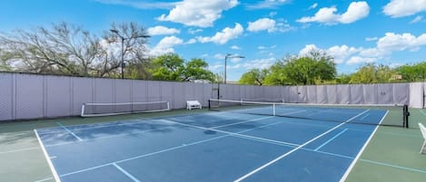 Un court de tennis avec un filet, entouré d’une clôture, sous un ciel dégagé.