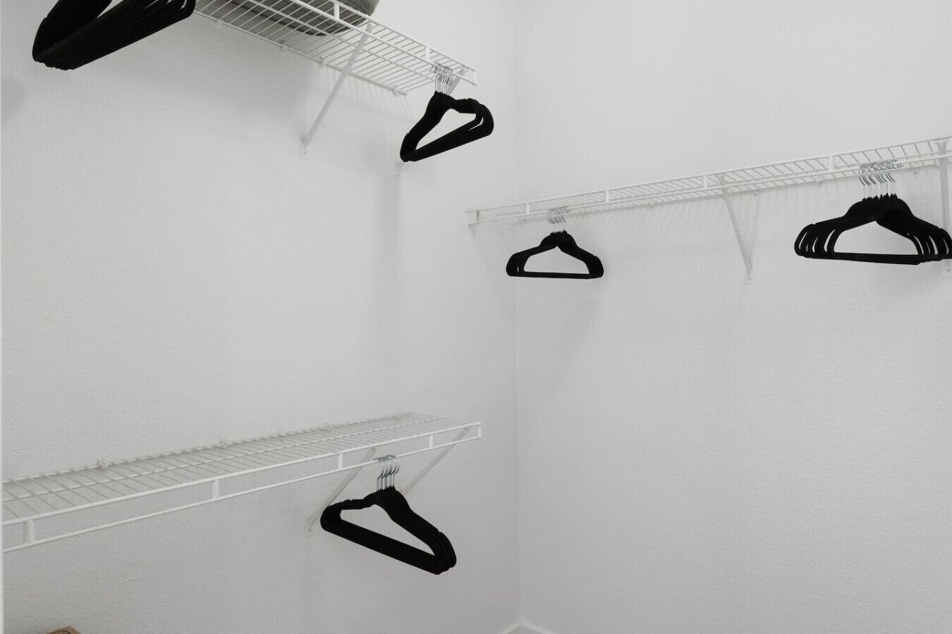 Quarto com paredes brancas, um porta-roupas de metal e uma prateleira de metal.