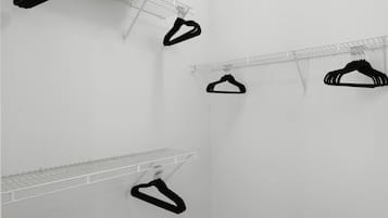 Quarto com paredes brancas, um porta-roupas de metal e uma prateleira de metal.