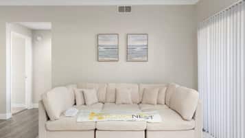 Una sala de estar con un sofá color beige, dos cuadros en la pared y una puerta blanca.